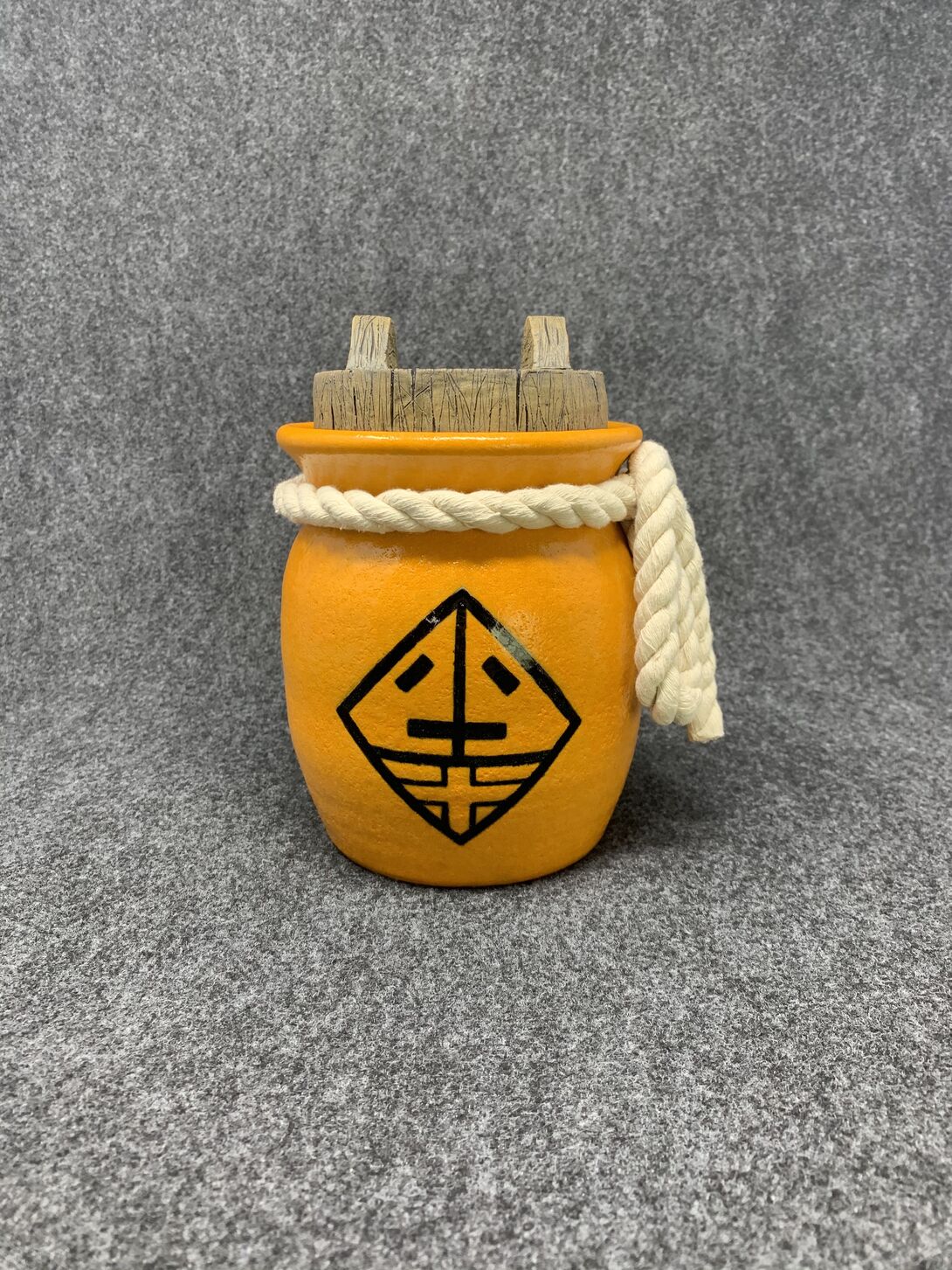 A bright orange funeral urn with a rope wrapped around its neck and a black graphic design on its front